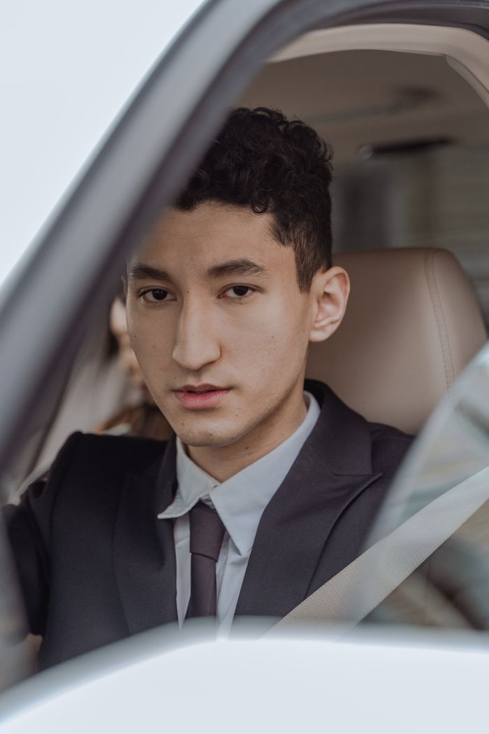 Portrait of an Asian man in a suit with an elegant demeanor, inside a car looking at the camera.